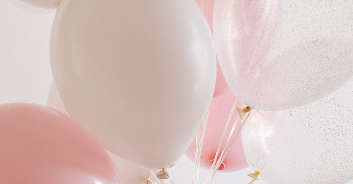 A pastel pink and white balloon bouquet held by a hand against a light background, ideal for celebrations.